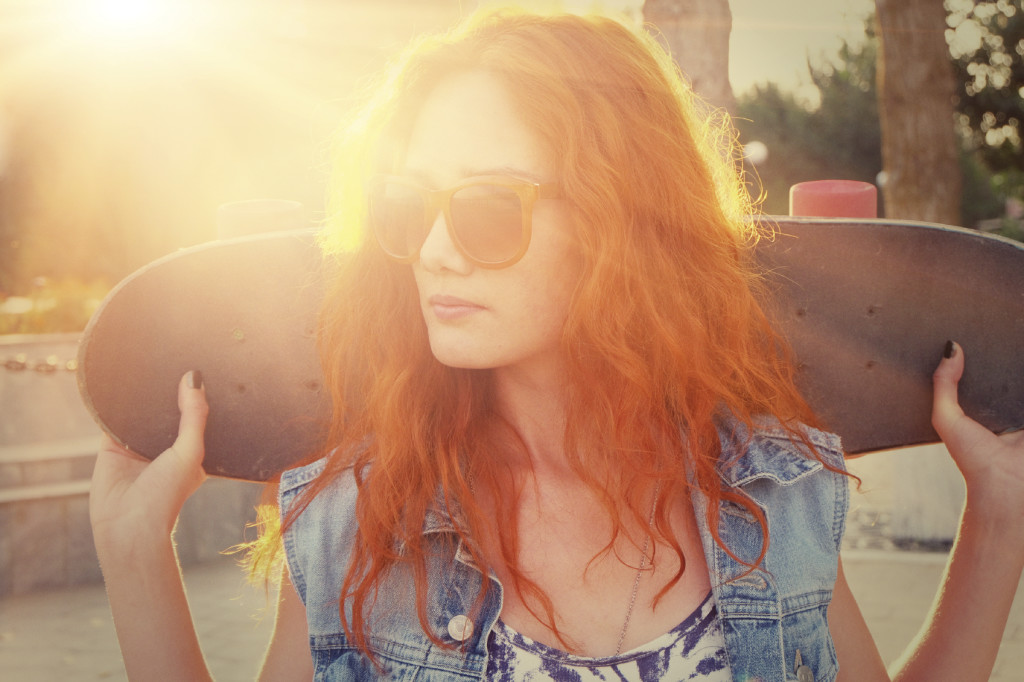 A young woman is standing in the street holding skateboard behind her head. Outdoors. Street fashion  lifestyle.