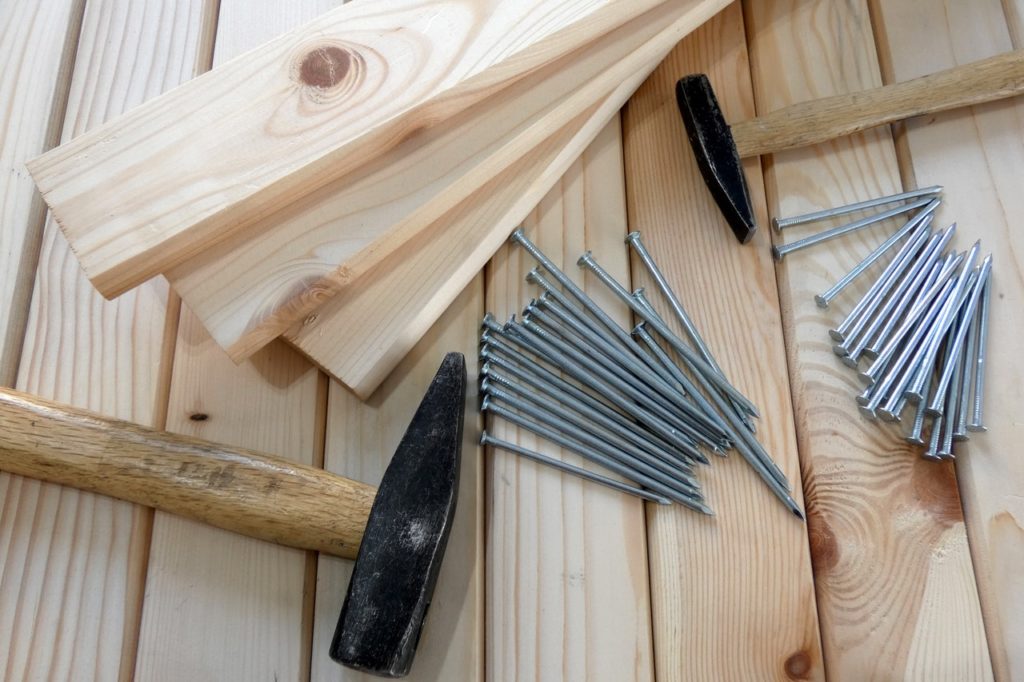 Gray nails beside two hammers and wooden planks